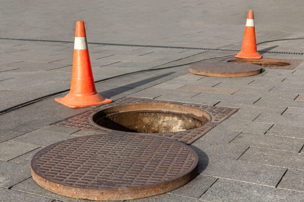 Manhole cover open in street and repair of roads. Accident with sewer hatch in city. Concept of repair of sewage, underground utilities, water supply system, cable laying.